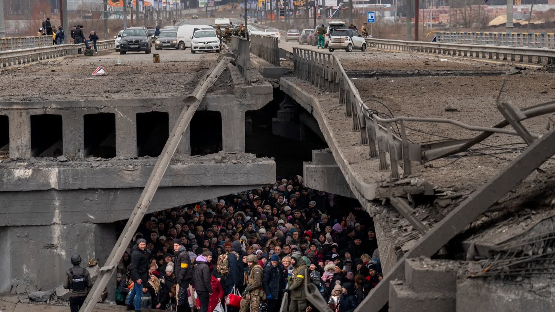 photo by By Emilio Morenatti, people crowd under a bridge as they try to flee across the Irpin River